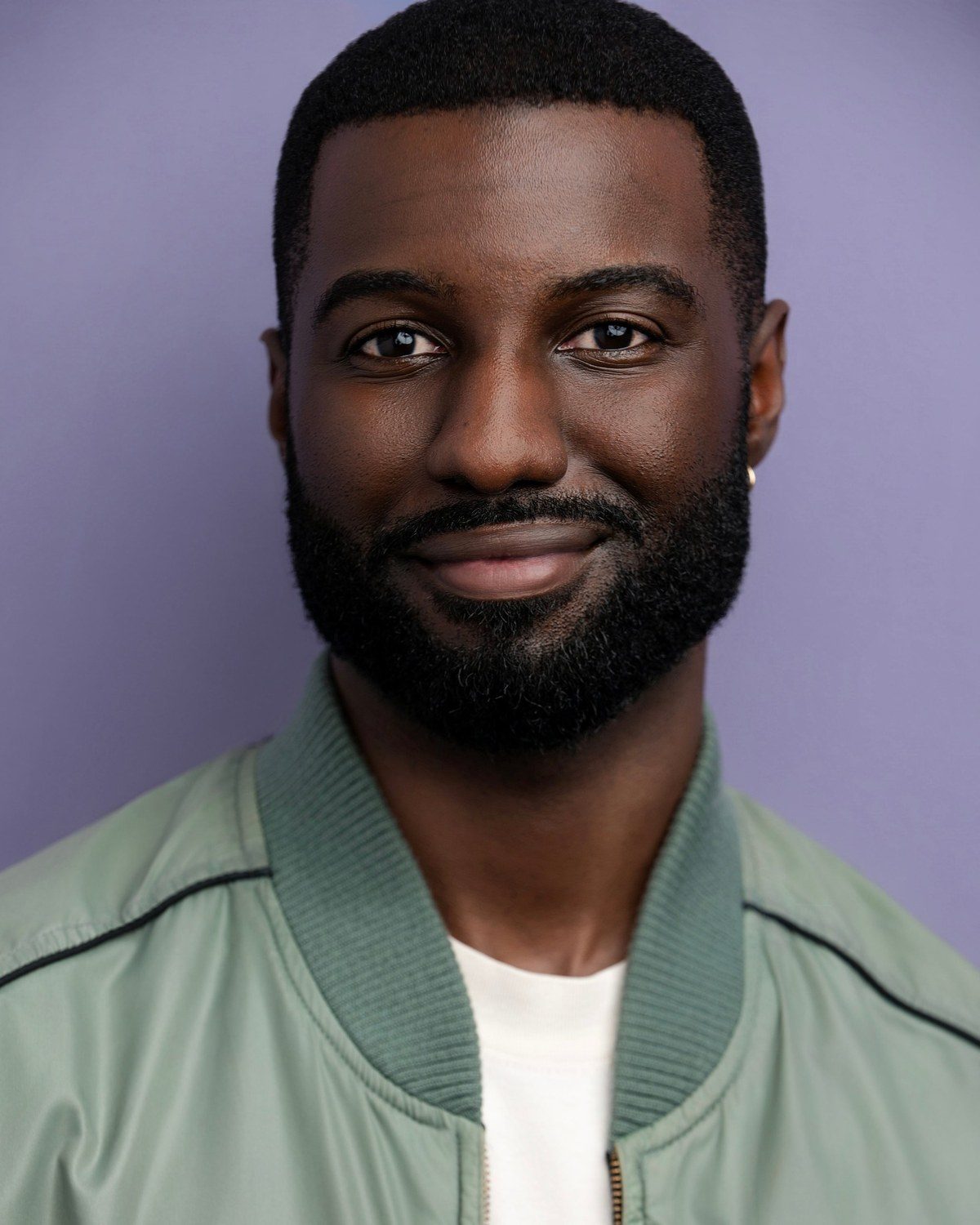 Marcus R. Smith smiling headshot, green jacket on a lavender background