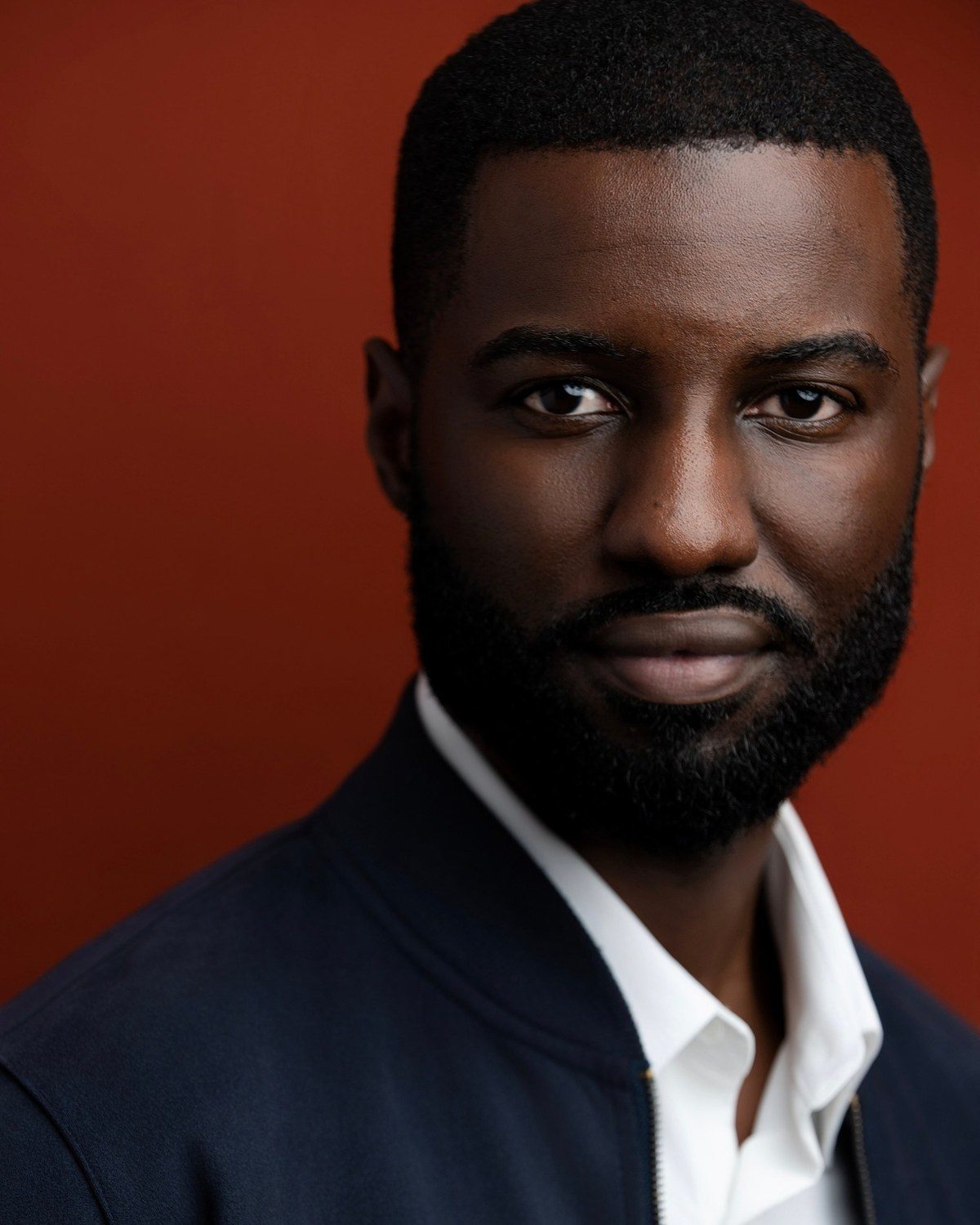 Marcus R. Smith headshot, navy jacket on a rust background